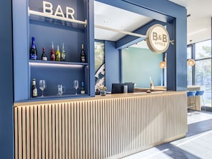 A modern bar area with a blue color scheme, a wooden counter, and a variety of bottles and glasses. - B&B Hotel München-Trudering (Munich)
