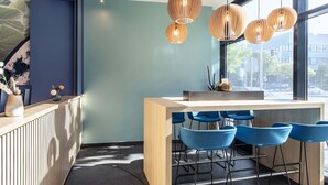 Zona de bar moderna con mostrador de madera, taburetes azules e iluminación colgante.