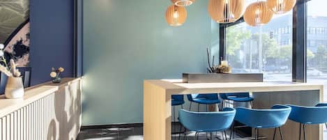 Zona de bar moderna con mostrador de madera, taburetes azules e iluminación colgante.