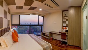 A modern hotel room with a large bed, a desk, and a view of the city at dusk. - Hotel Parami (Yangon)