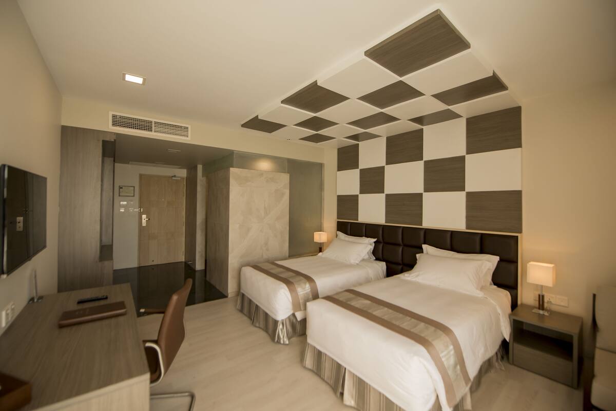 Ein Hotelzimmer mit zwei Betten, einem Schreibtisch, einem Sessel und einem Fernseher.