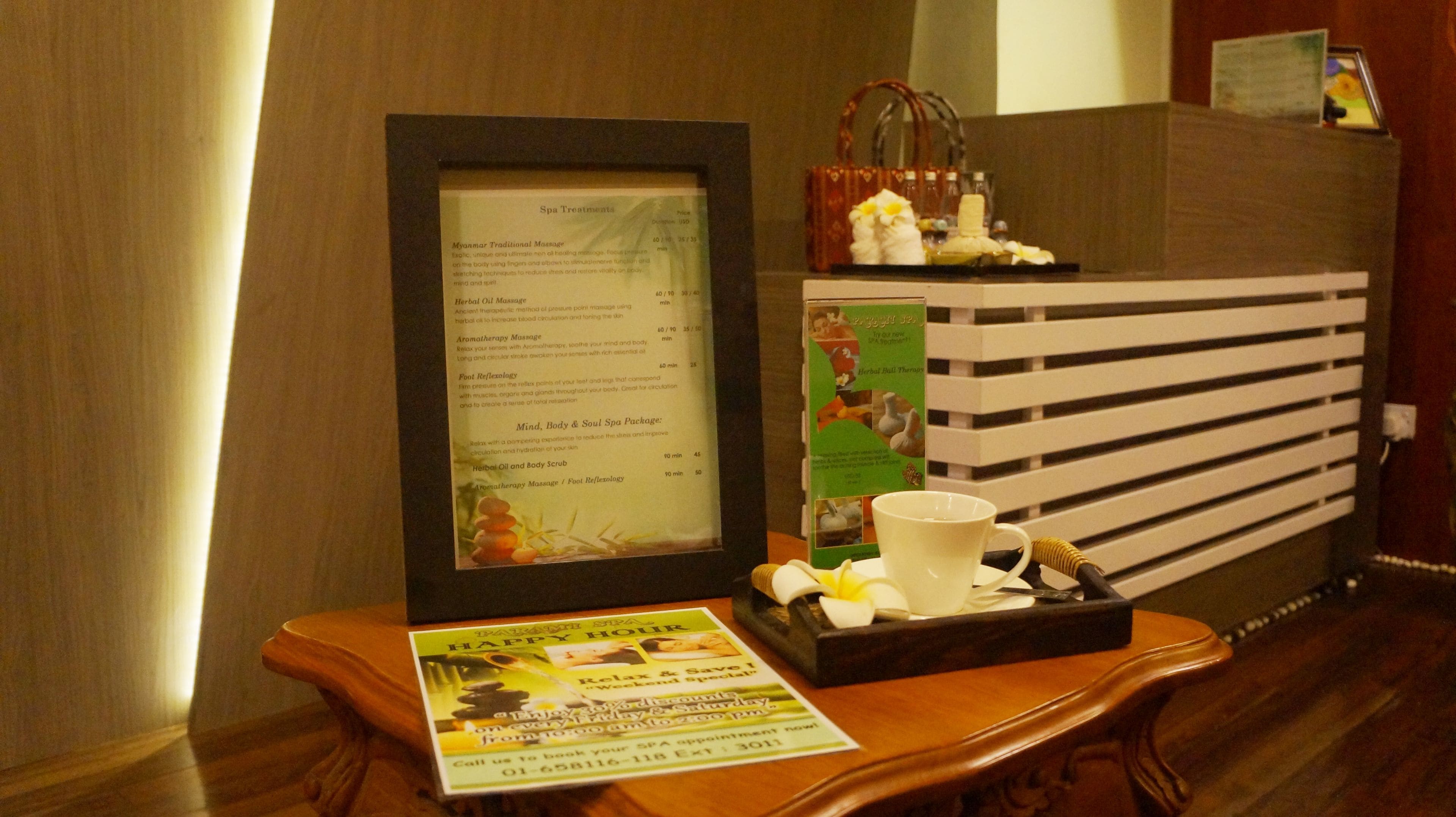 A reception desk with a framed menu, a small table with a cup and a tray, and a poster advertising spa services.