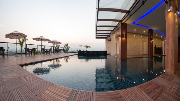 A rooftop pool area with lounge chairs and umbrellas, a glass-enclosed bar, and a view of the city skyline. - Hotel Parami (Yangon)