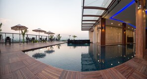 A rooftop pool area with lounge chairs and umbrellas, a glass-enclosed bar, and a view of the city skyline. - Hotel Parami (Yangon)