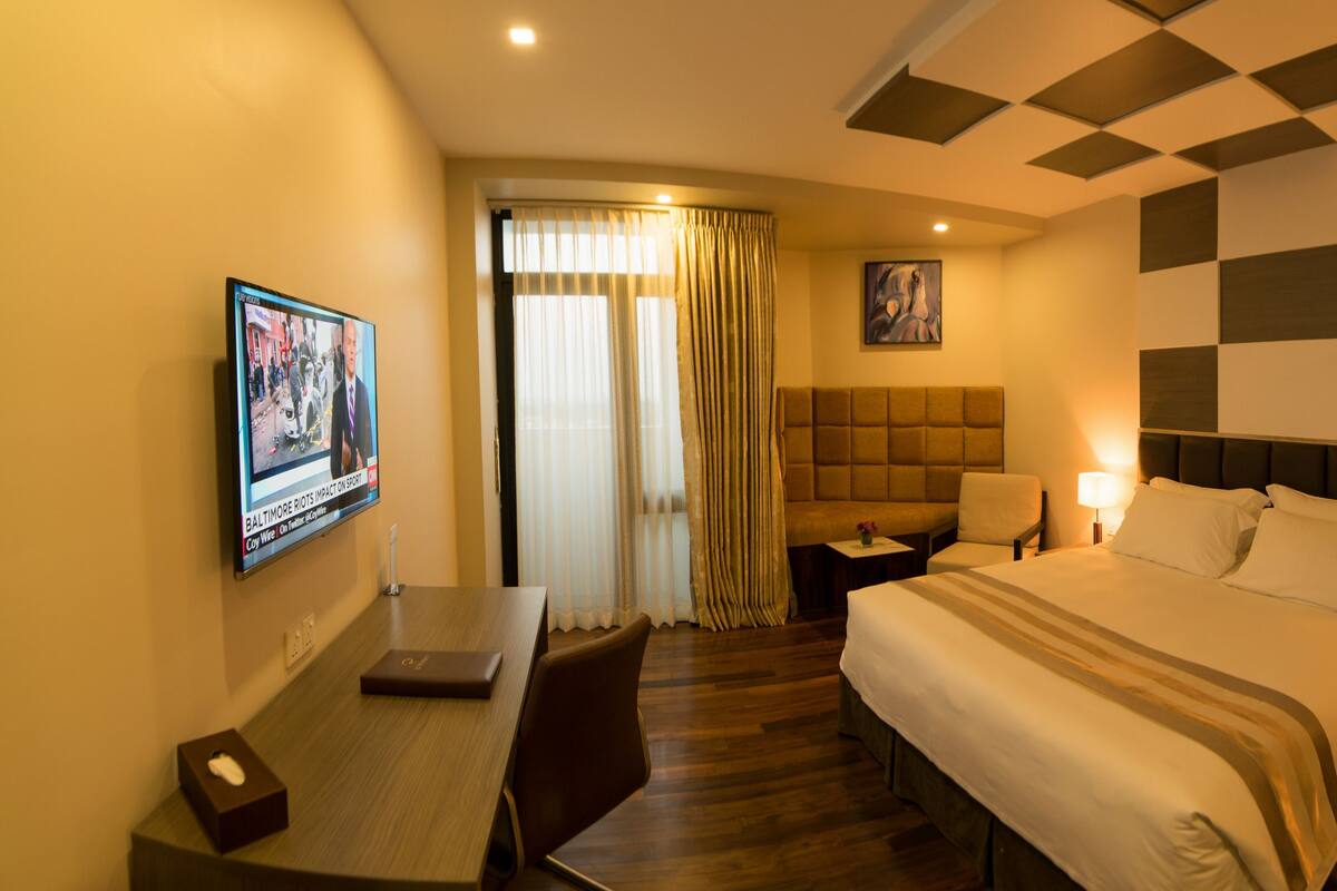 Ein Hotelzimmer mit Bett, Schreibtisch, Stuhl, Fernseher und einem Bild an der Wand.