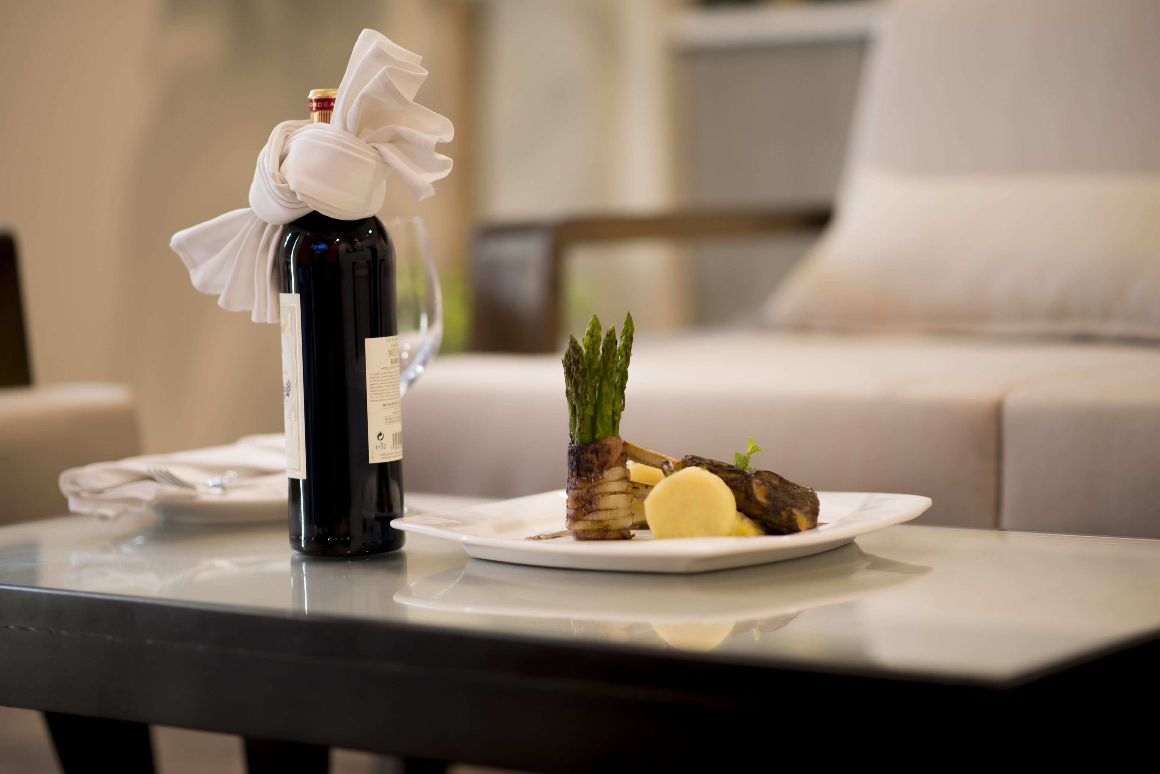 A dining table with a bottle of wine, a plate with asparagus and a piece of meat, and a white napkin.