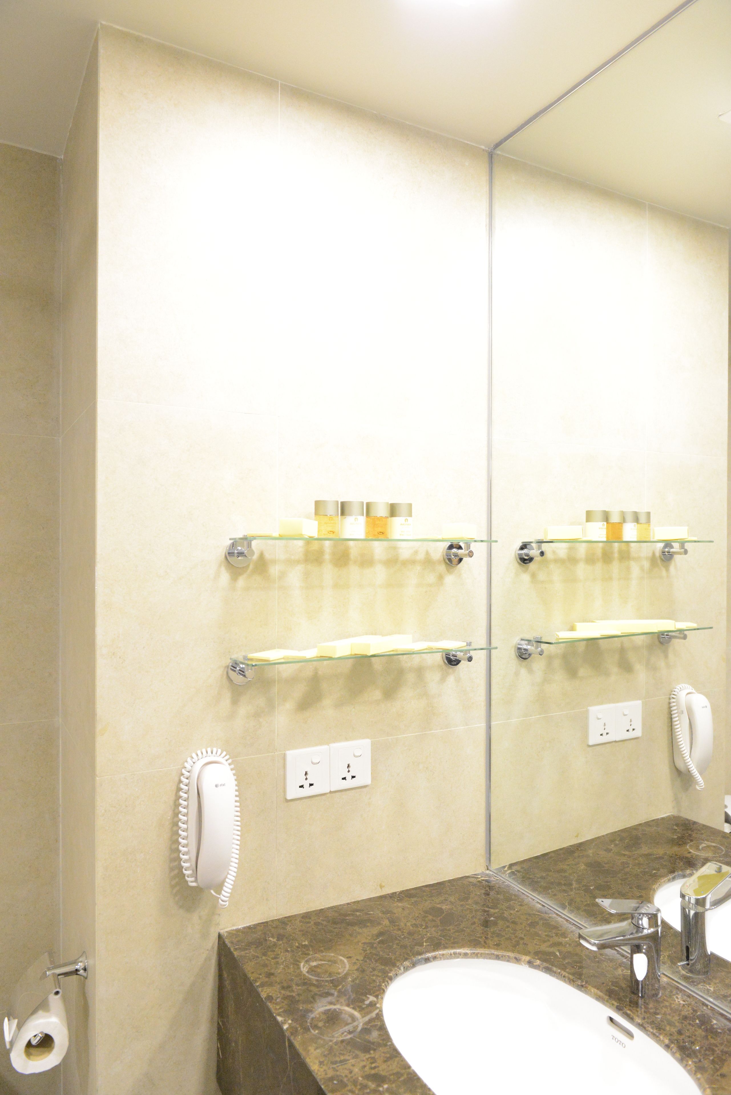 A bathroom with a marble sink, a mirror, and a glass shelf with toiletries.