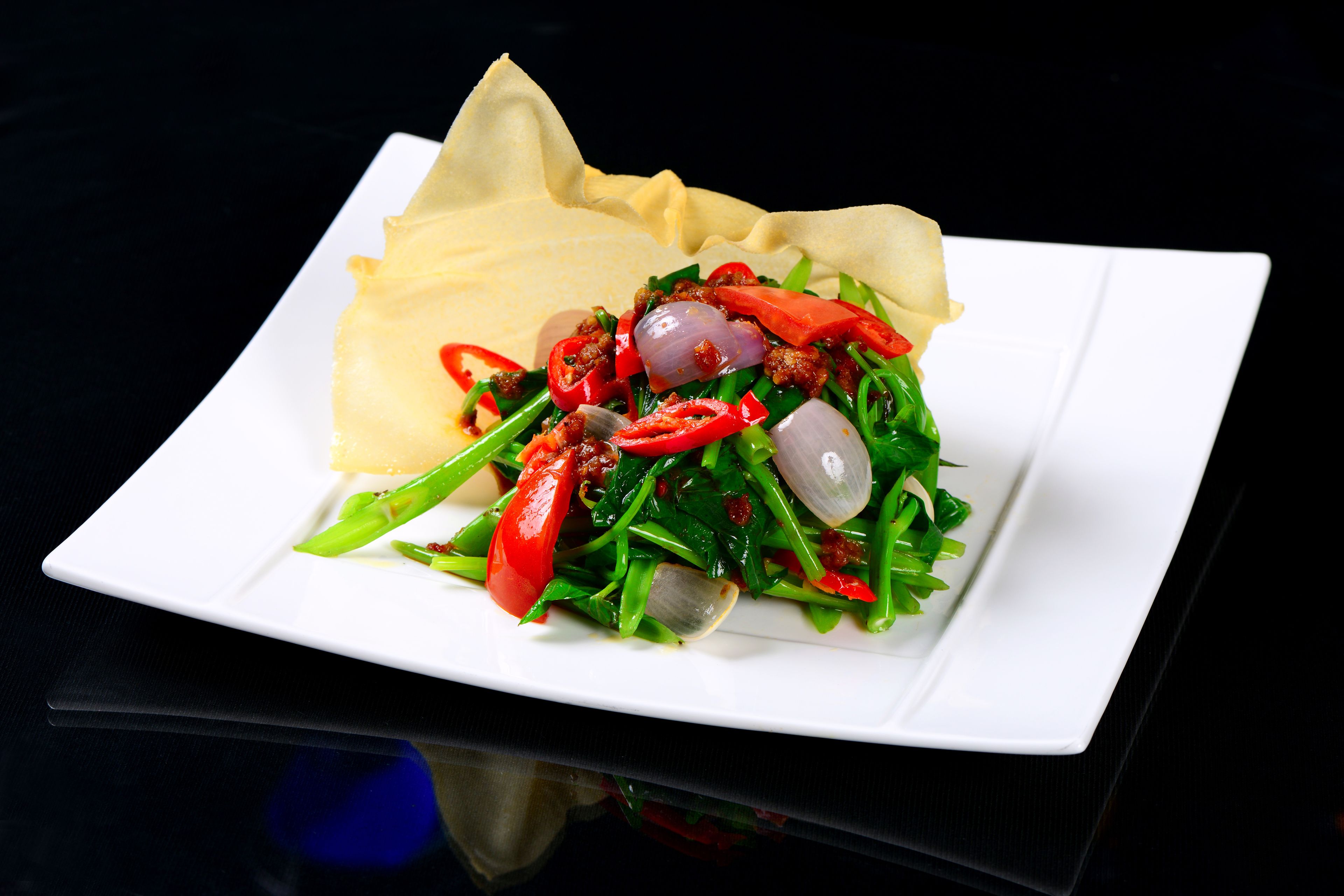 A white plate with a salad, red peppers, green beans, and onions.