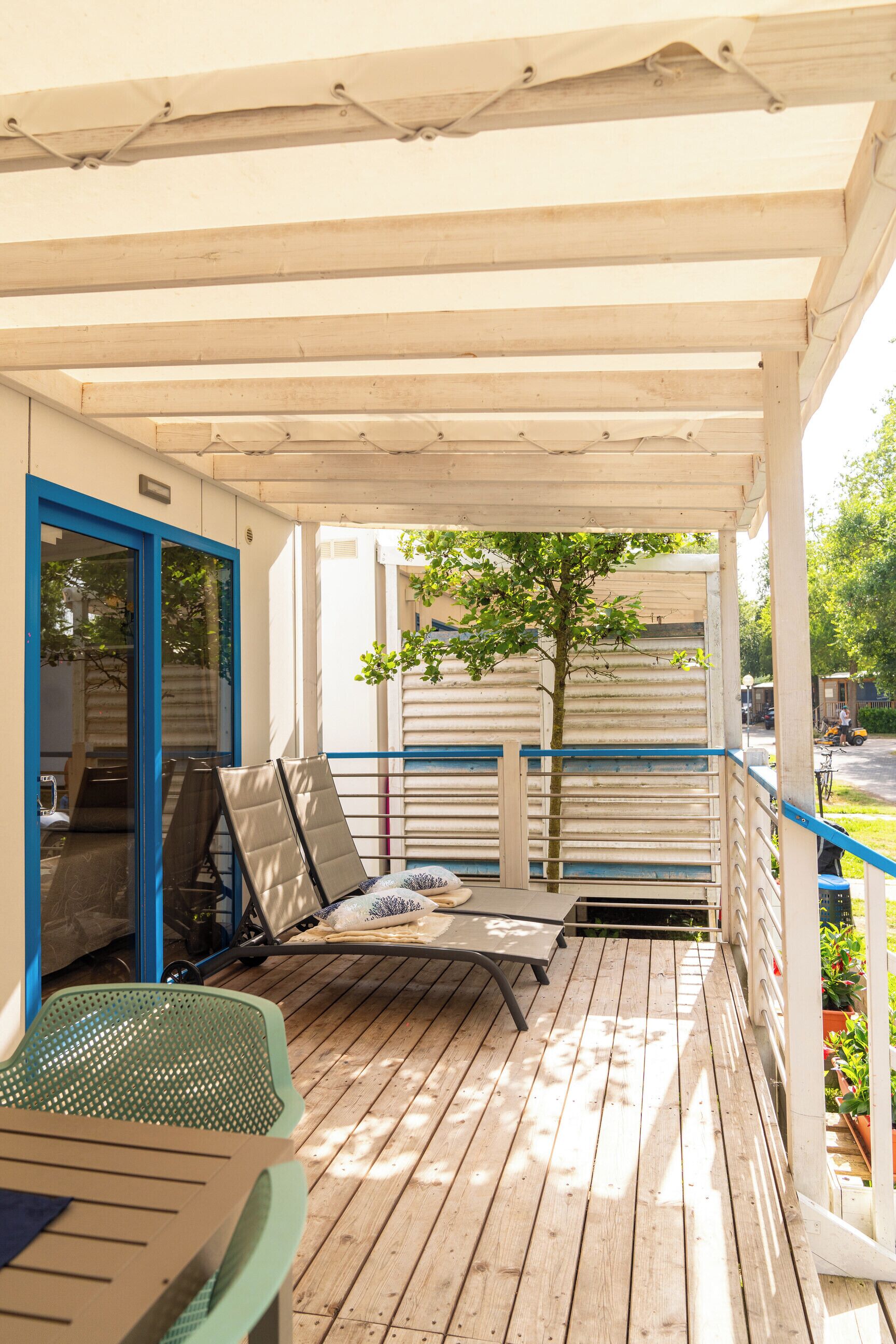 A covered outdoor area with a wooden deck, a blue-framed door, and a small table with a chair.
