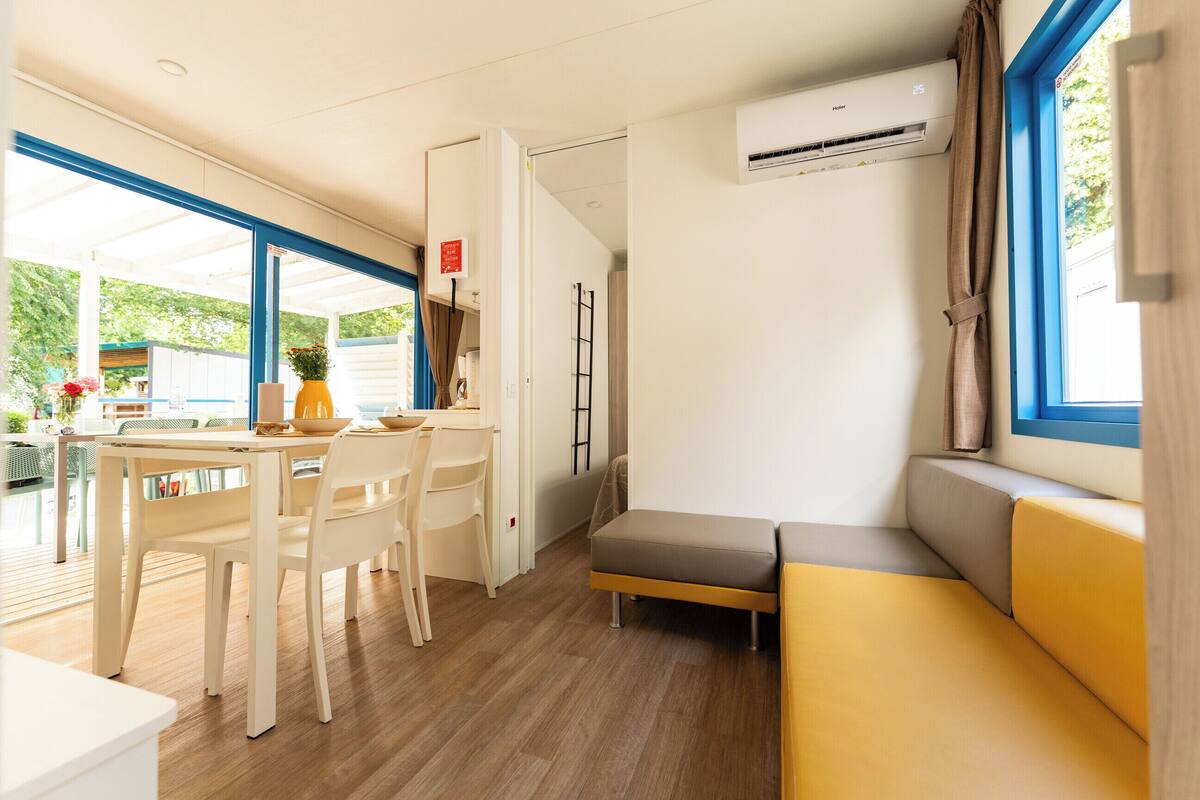 A modern, well-lit room with a dining area, a sofa, and an air conditioning unit.
