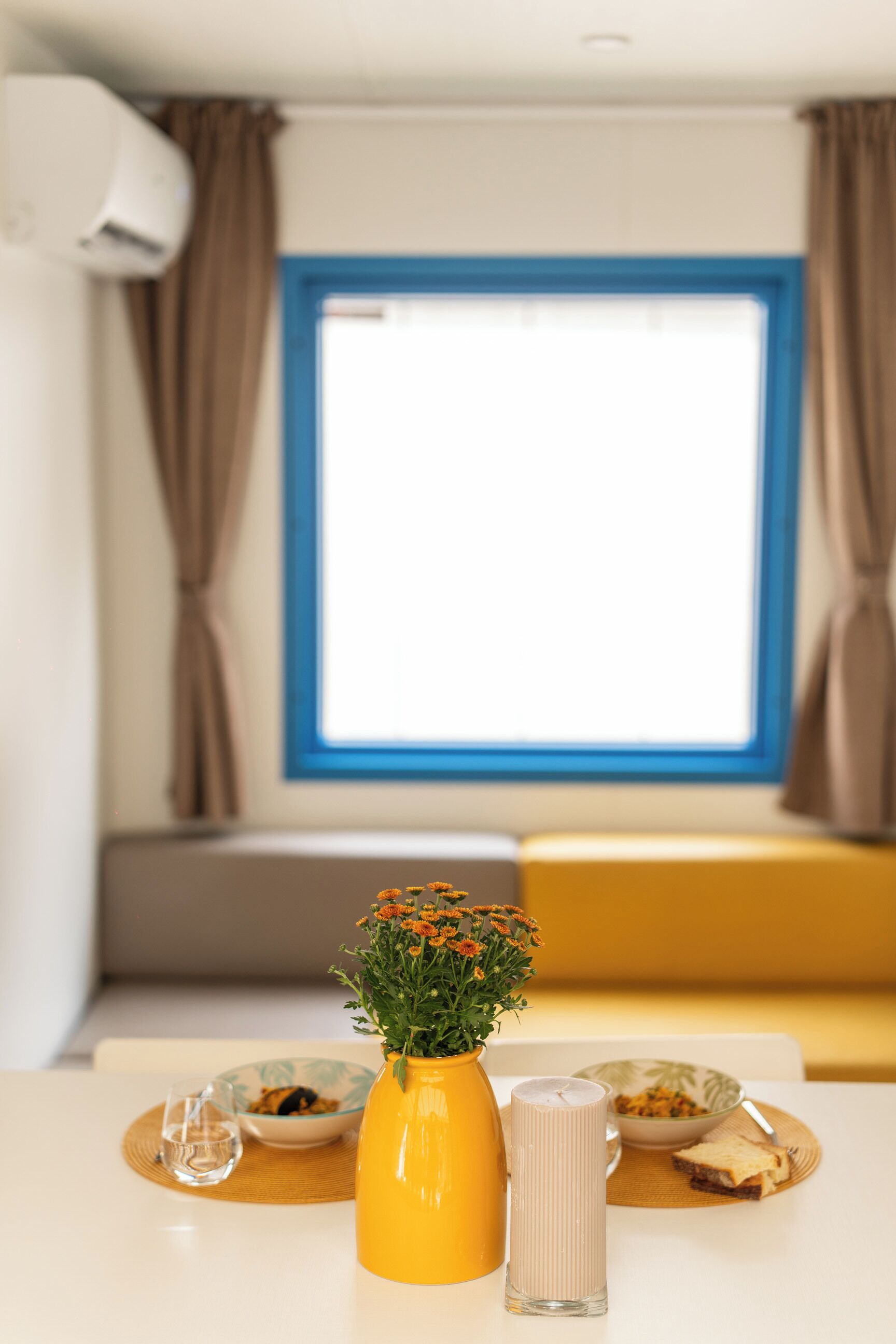 Een eettafel met een gele vaas, een glas en een schaal met eten.
