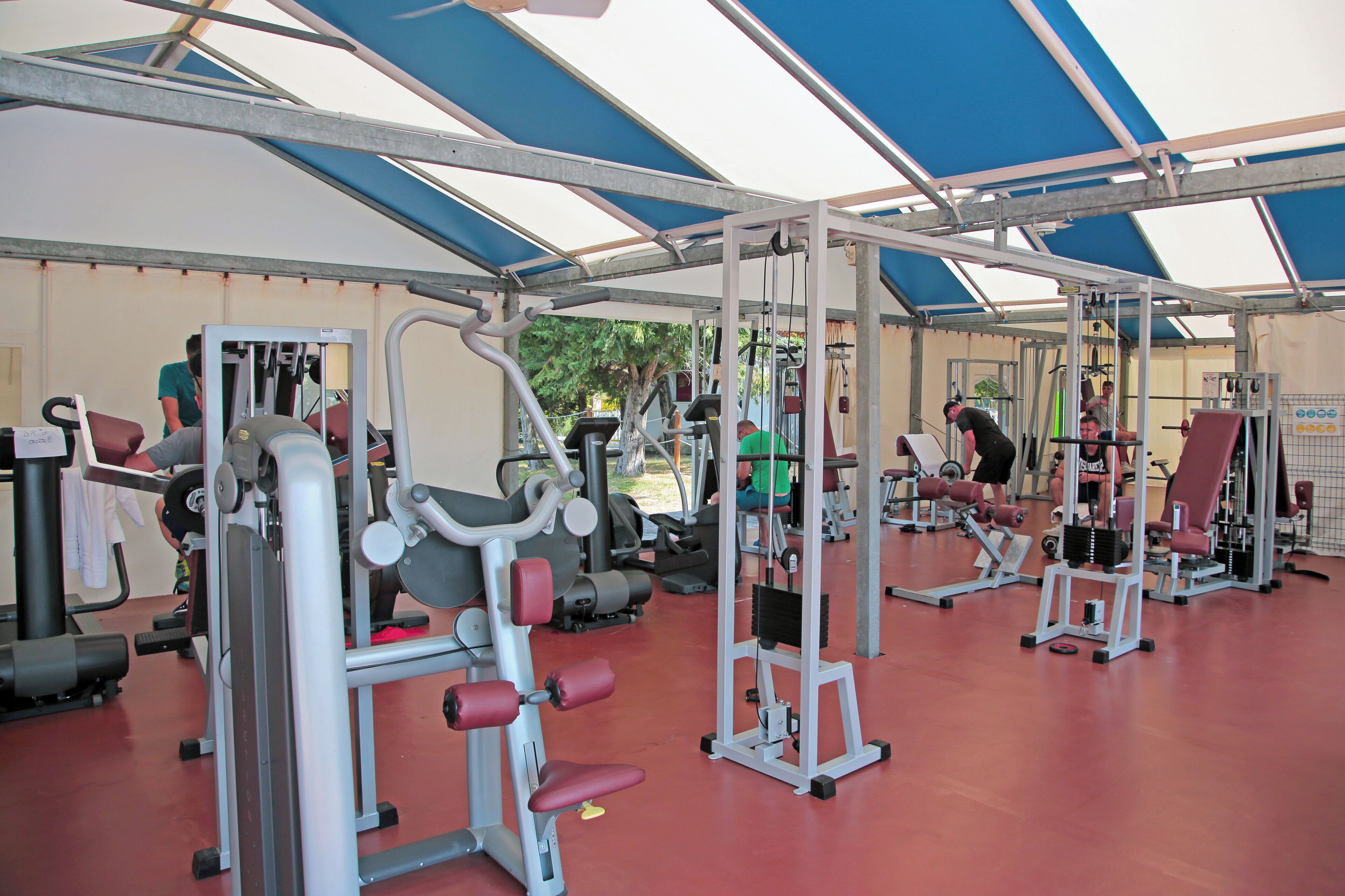 Een fitnessruimte met diverse trainingsapparaten en een overdekt gedeelte.