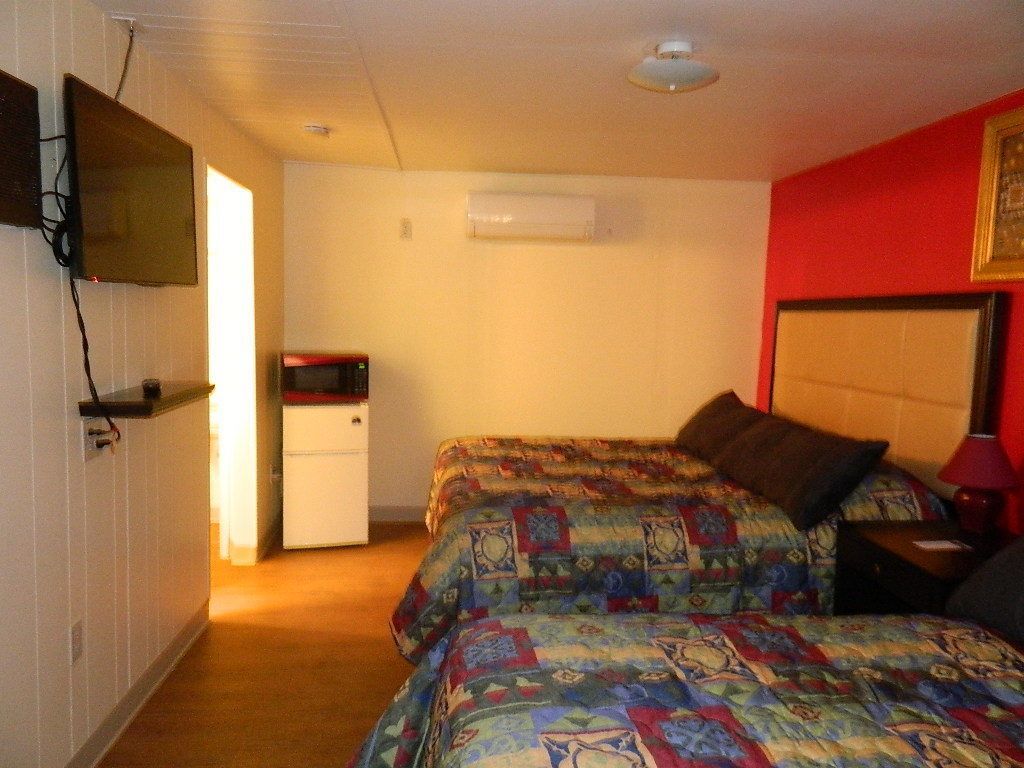 Un dormitorio con dos camas, un televisor montado en la pared, una kitchenette pequeña y una pared de acento roja.