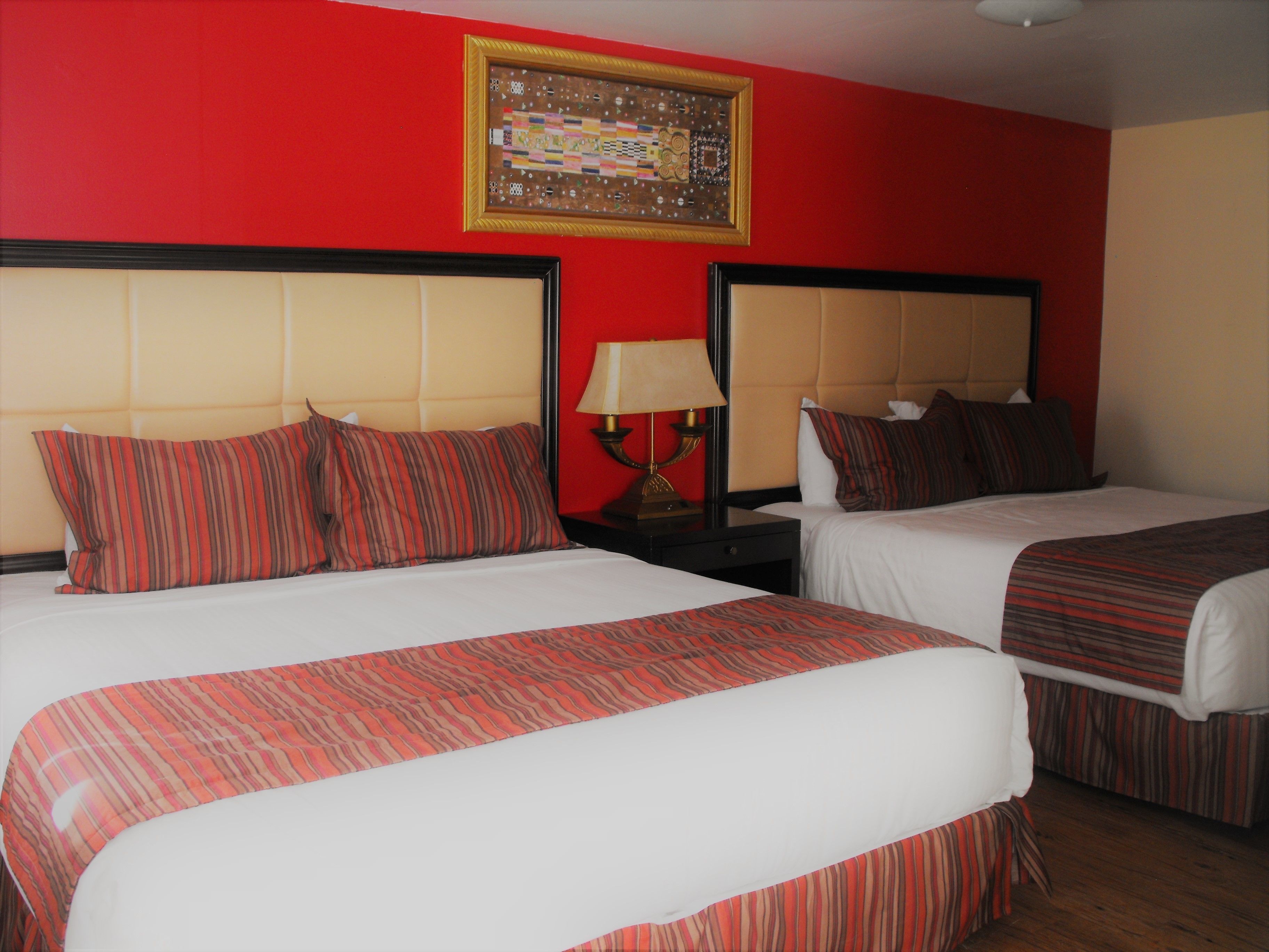 Two beds with striped bedding, a nightstand with a lamp, and a framed artwork on the wall.