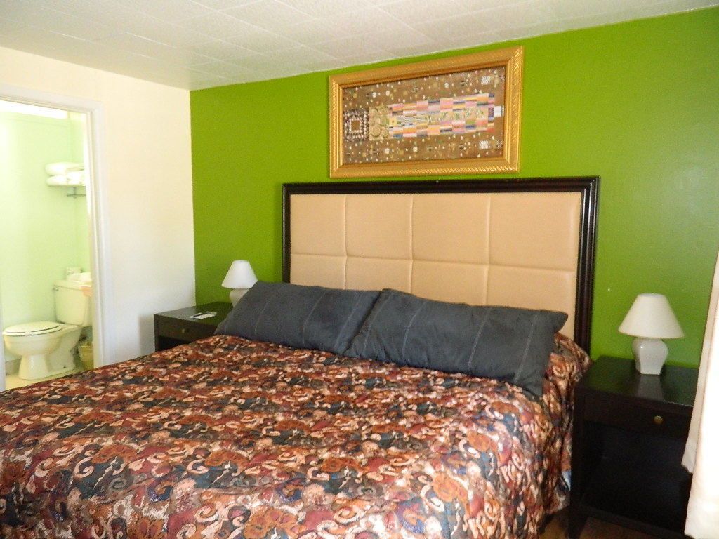 A bedroom with a patterned bedspread, a headboard, two bedside tables with lamps, and a framed picture on the wall.