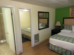 A hotel room with two beds, a mirror, a nightstand, and a door leading to another room.