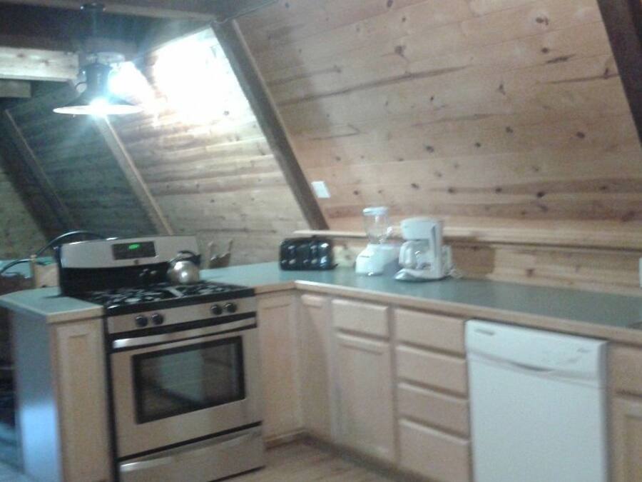 Een keuken met een gasfornuis, oven en vaatwasser. Er is een raam met gordijnen en een plafondventilator.