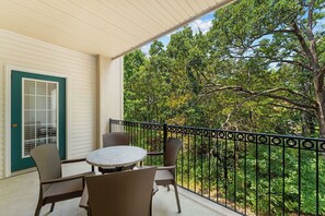 A balcony with a table and chairs, a door with a window, and a view of trees. - French Quarter Resort (Branson)