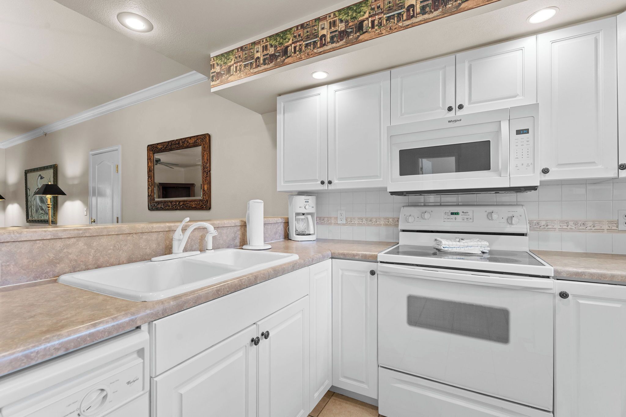 A kitchen with white cabinets, a double sink, a microwave, and a stove.