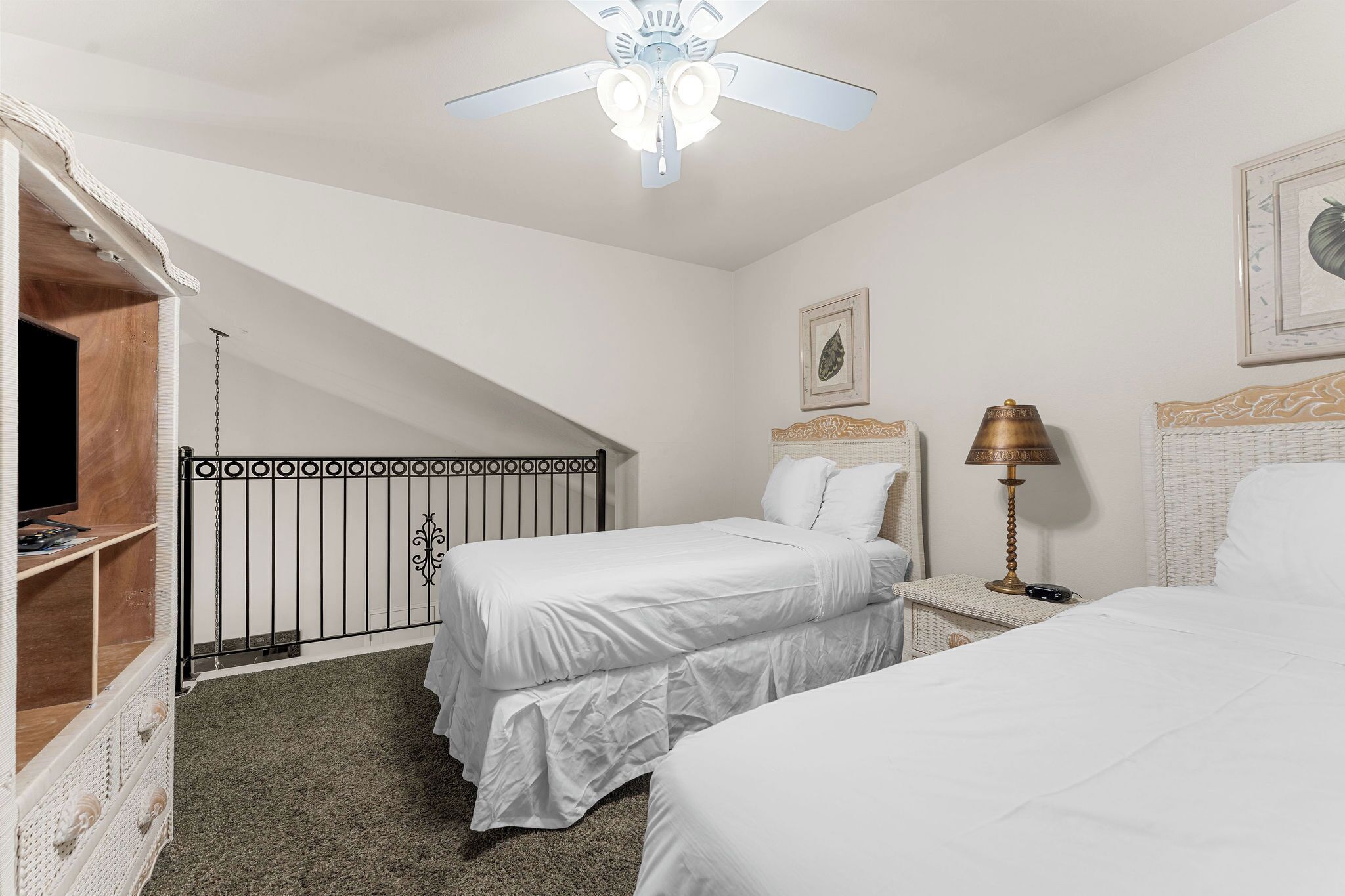 Una camera da letto con due letti, un ventilatore a soffitto, una lampada e un quadro appeso al muro.