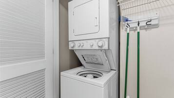 Ein kleiner Waschbereich mit einer Frontlader-Waschmaschine und einem Trockner, einem Wäscheständer und einem an der Wand befestigten Handtuchhalter.
