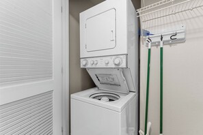 A compact laundry area with a front-loading washer and dryer, a drying rack, and a wall-mounted towel rack. - French Quarter Resort (Branson)