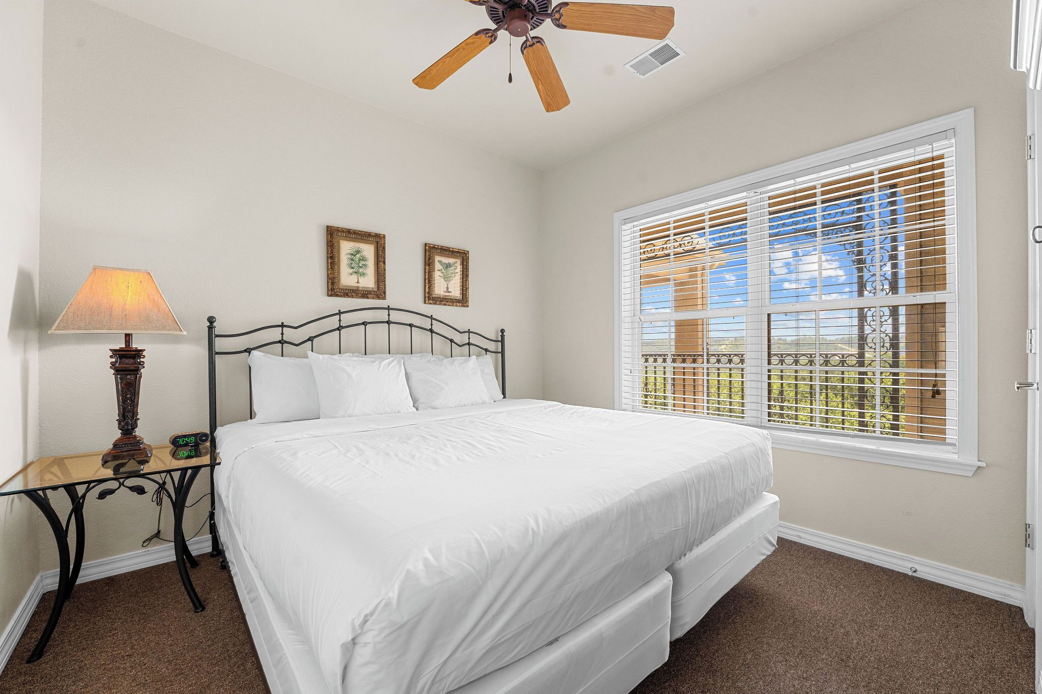 A bedroom with a bed, a nightstand, a lamp, a ceiling fan, and a window with blinds.