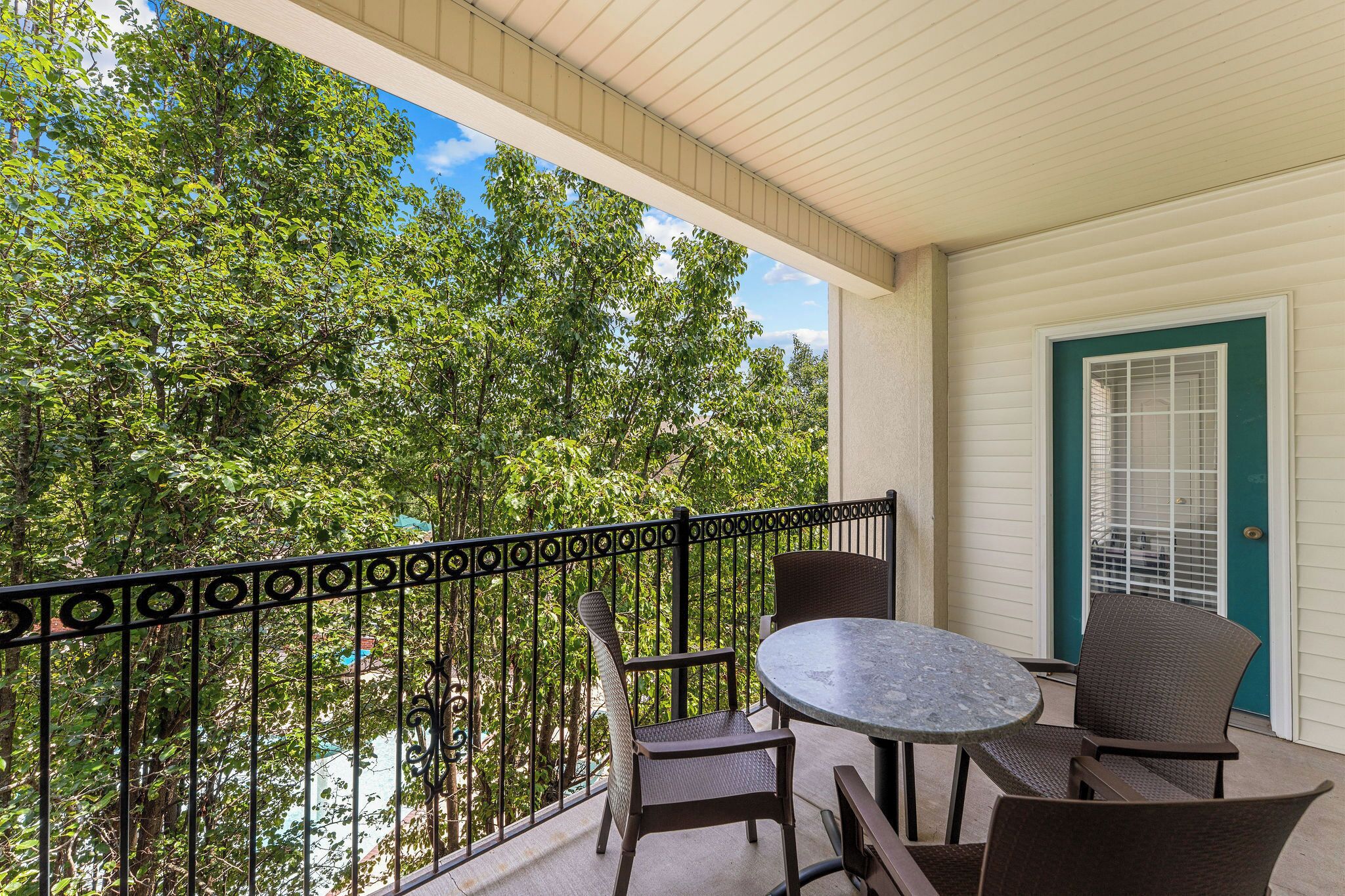 Un balcon avec une table et des chaises, une porte avec une fenêtre et une vue sur les arbres.