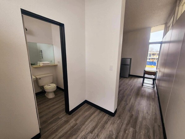 A narrow hallway with a wooden floor, leading to a bathroom with a toilet and a mirror. - The Hastings Inn Salina (Salina)