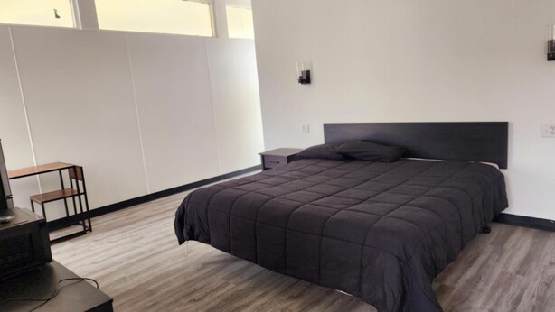 Un dormitorio moderno con una cama grande, una mesita de noche, un escritorio con una silla y una ventana que proporciona luz natural.