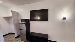 Un espacio habitable compacto con un televisor de pantalla plana montado en la pared, microondas integrado y refrigerador.