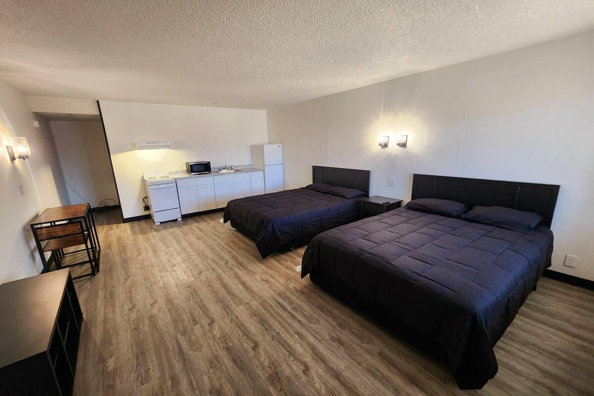 A hotel room with two beds, a kitchenette, and a small dining area.