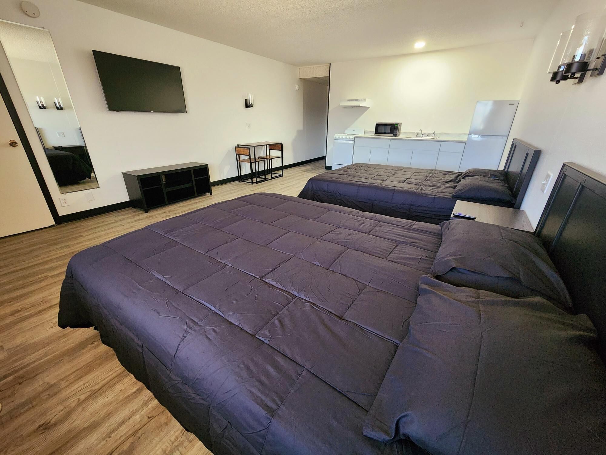 Una camera d'albergo moderna con due letti, una televisione a schermo piatto, un angolo cottura e un'area salotto con poltrone.