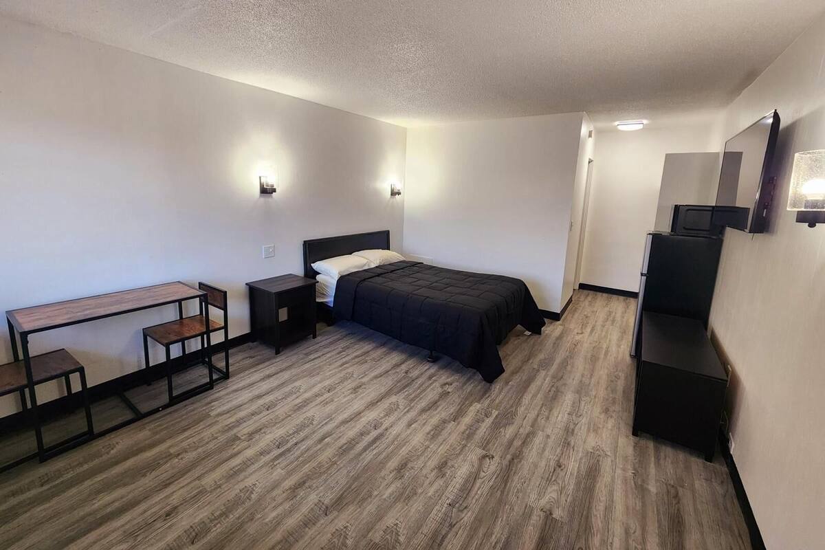 A bedroom with a bed, a desk, and a chair. There are wall-mounted lights and a mirror.