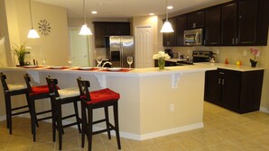 A modern kitchen with dark cabinets, a large island with bar stools, stainless steel appliances, and pendant lighting. - Crystal Cove by CozyKey Vacation Rentals (Kissimmee)