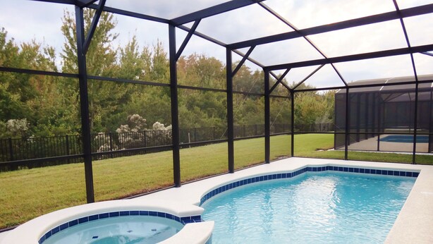 A swimming pool with a hot tub, surrounded by a covered area with a metal frame and glass walls. - Crystal Cove by CozyKey Vacation Rentals (Kissimmee)