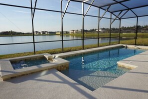 A swimming pool with a glass enclosure, clear water, and a view of a lake and houses in the background. - Crystal Cove by CozyKey Vacation Rentals (Kissimmee)