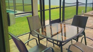 A covered patio with a glass table and chairs, overlooking a grassy area and a body of water. - Crystal Cove by CozyKey Vacation Rentals (Kissimmee)