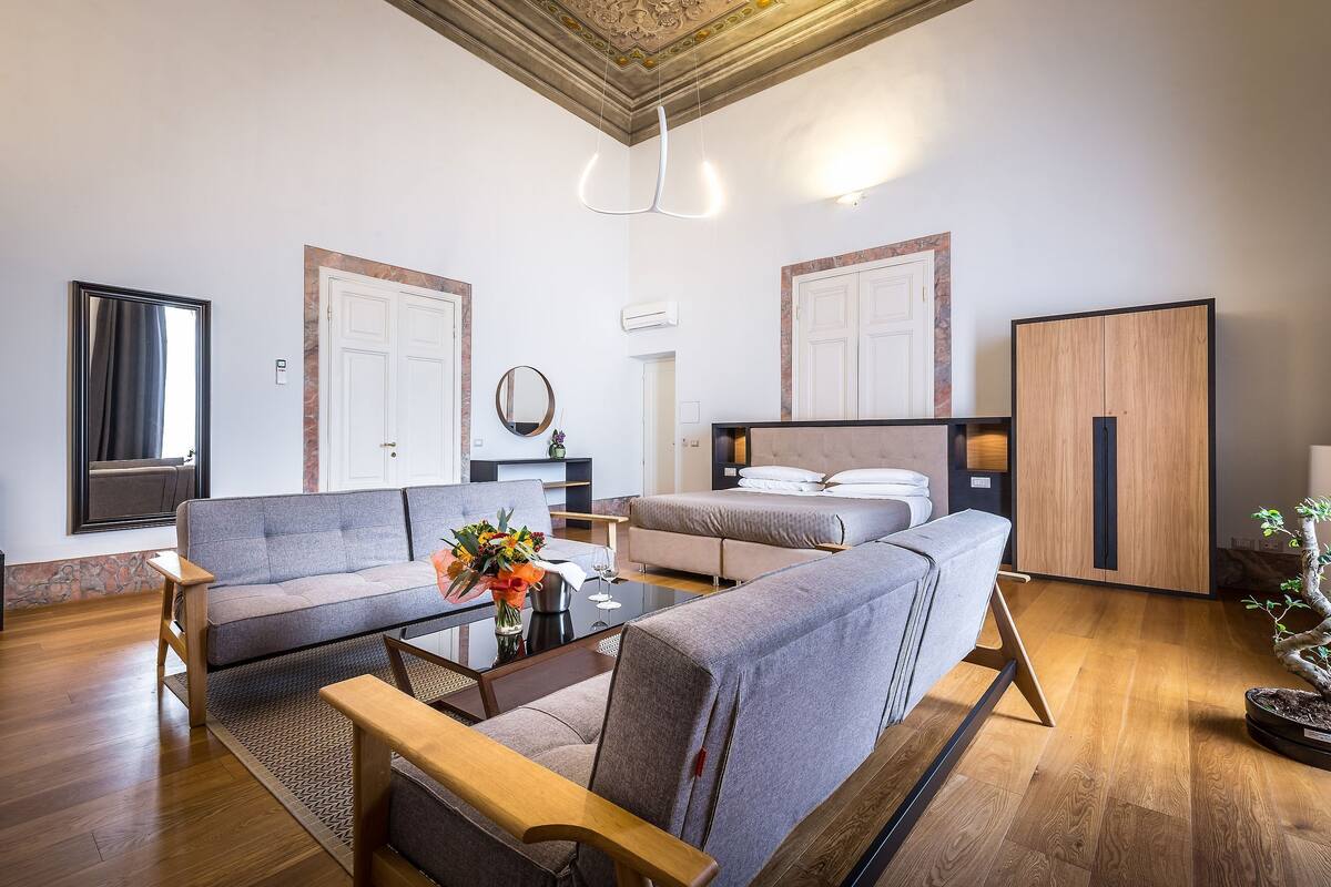 A modern living room with a sofa, armchairs, a coffee table, and a dining table. There are two doors, a mirror, and a cabinet.