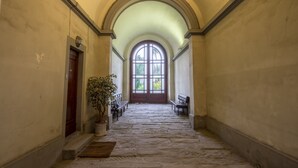 A corridor with stone flooring, benches, and a large arched window at the end. - Residenza D'Epoca Al Numero 8 (Florence)