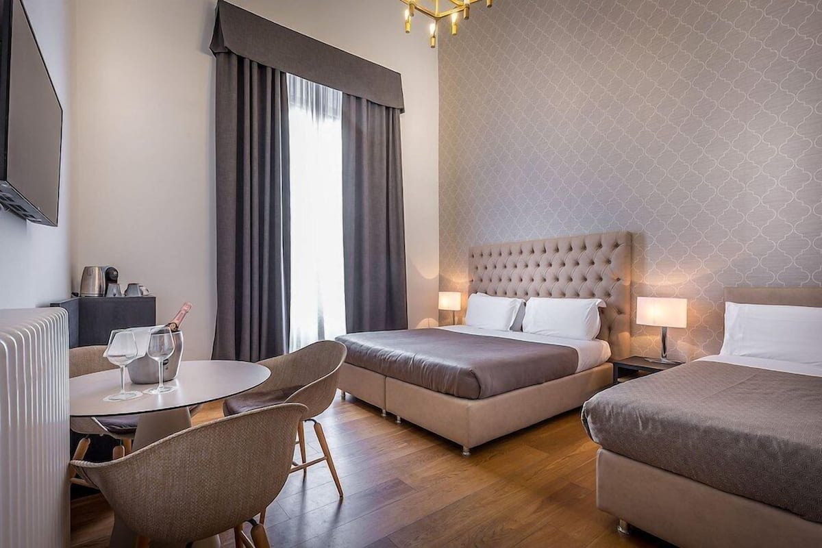 A hotel room with two beds, a dining area with a table and chairs, and a minibar.