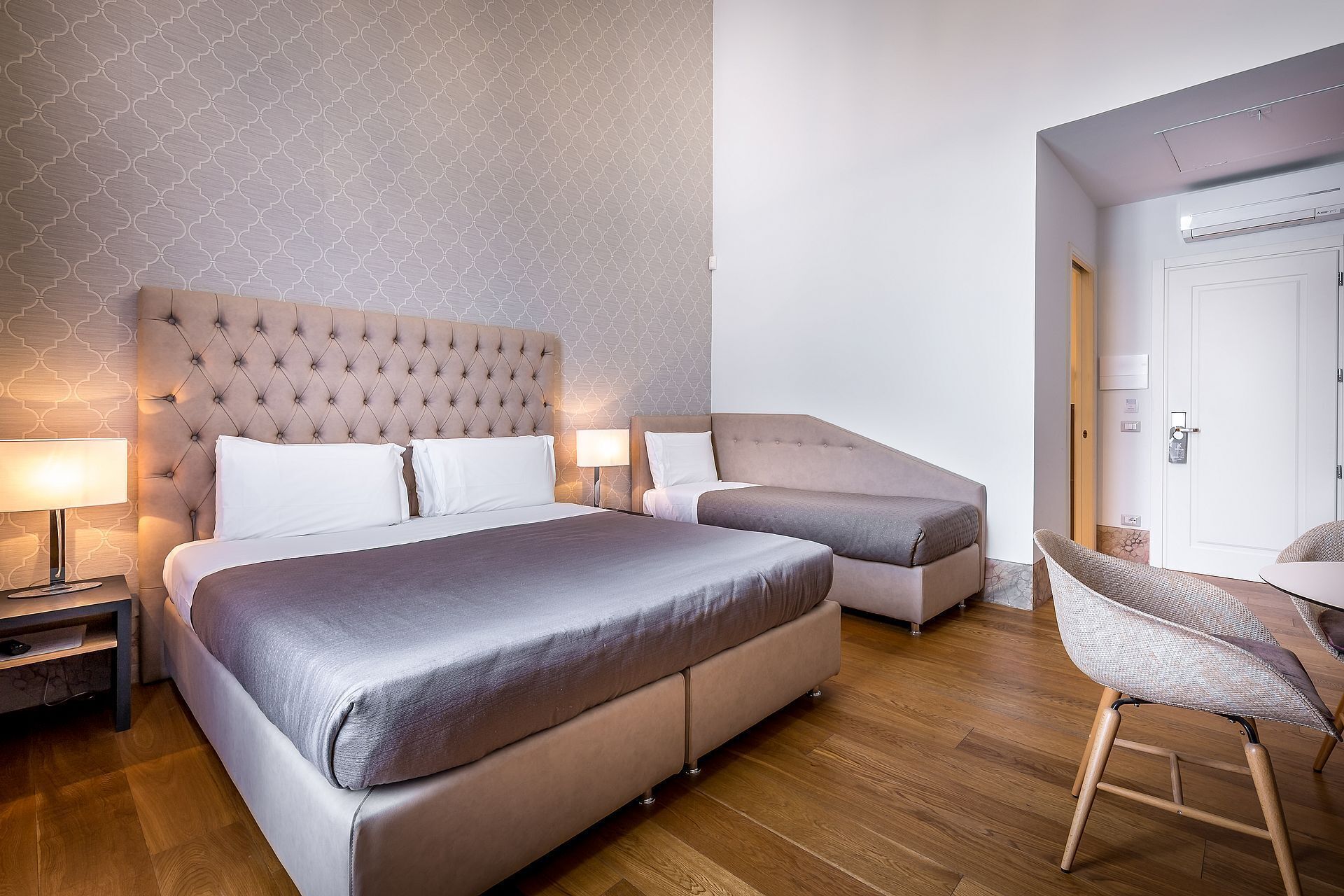 Een hotelkamer met een groot bed, twee nachtkastjes, een stoel en een deur met een handgreep.