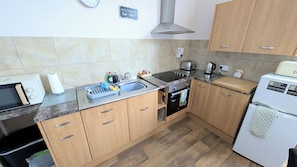 A kitchen with wooden cabinets, a sink, a toaster, a kettle, and a refrigerator. - Parterre Holiday Apartments (Sandown)