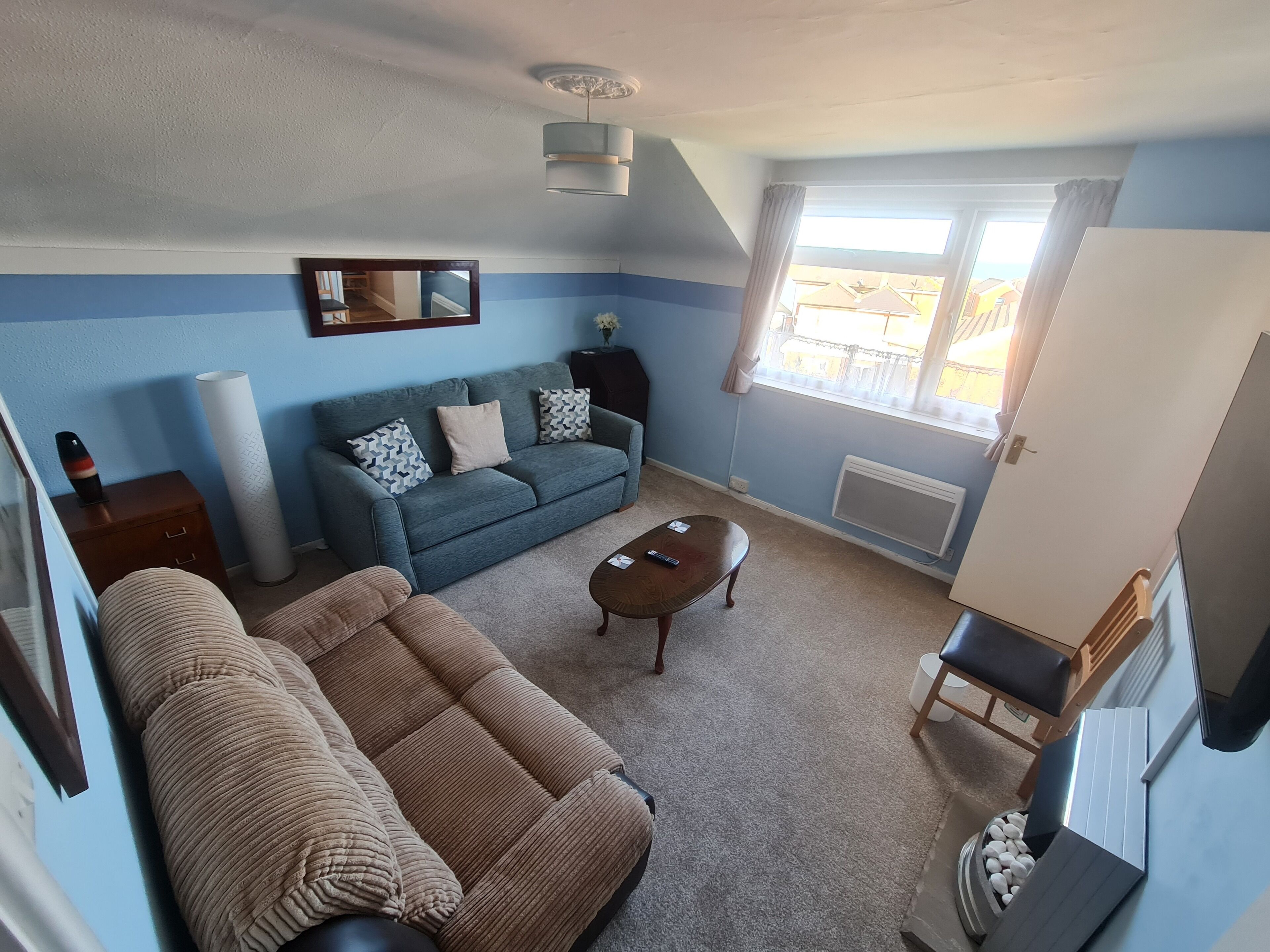 Una sala de estar con sofá, mesa de centro y televisor. Se ve una ventana con cortinas y un radiador.