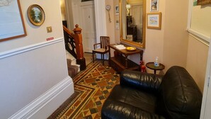A hallway with a black leather sofa, a wooden chair, a small table with a bowl, a mirror, and a staircase leading to another room. - Parterre Holiday Apartments (Sandown)