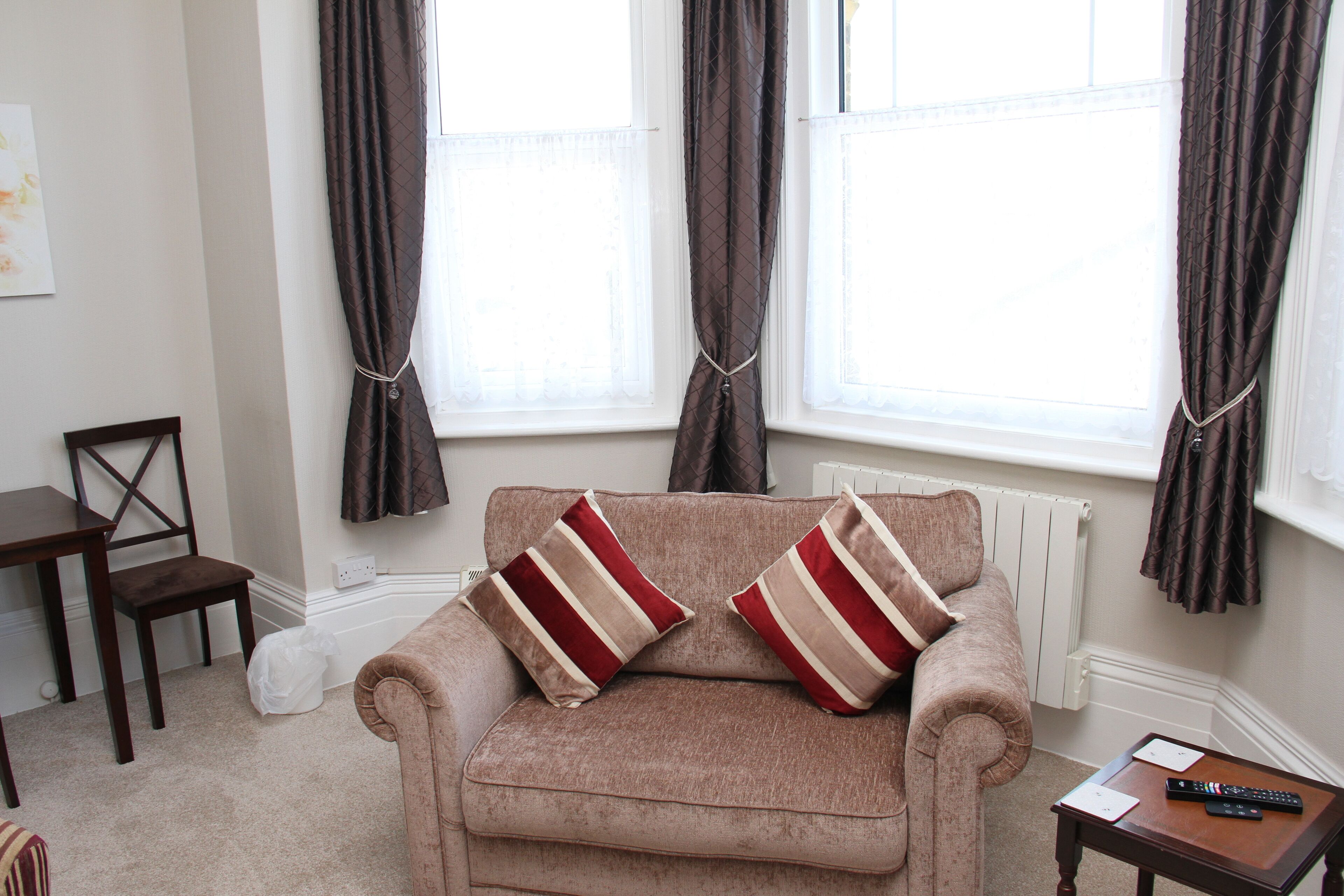 A living room with a beige sofa, two striped pillows, a wooden side table, and a chair.