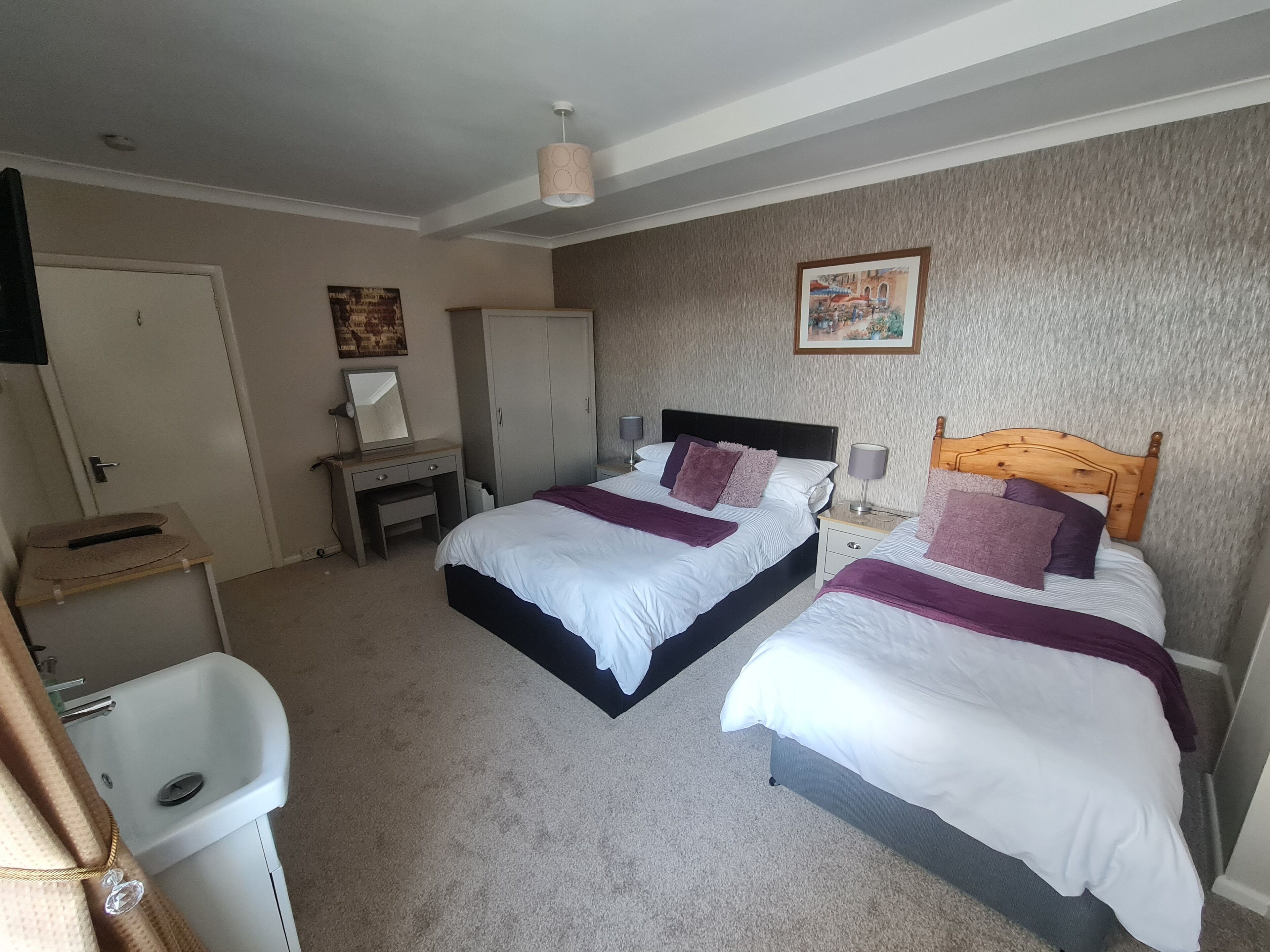 A bedroom with two beds, a desk, a chair, a wardrobe, and a bathroom.