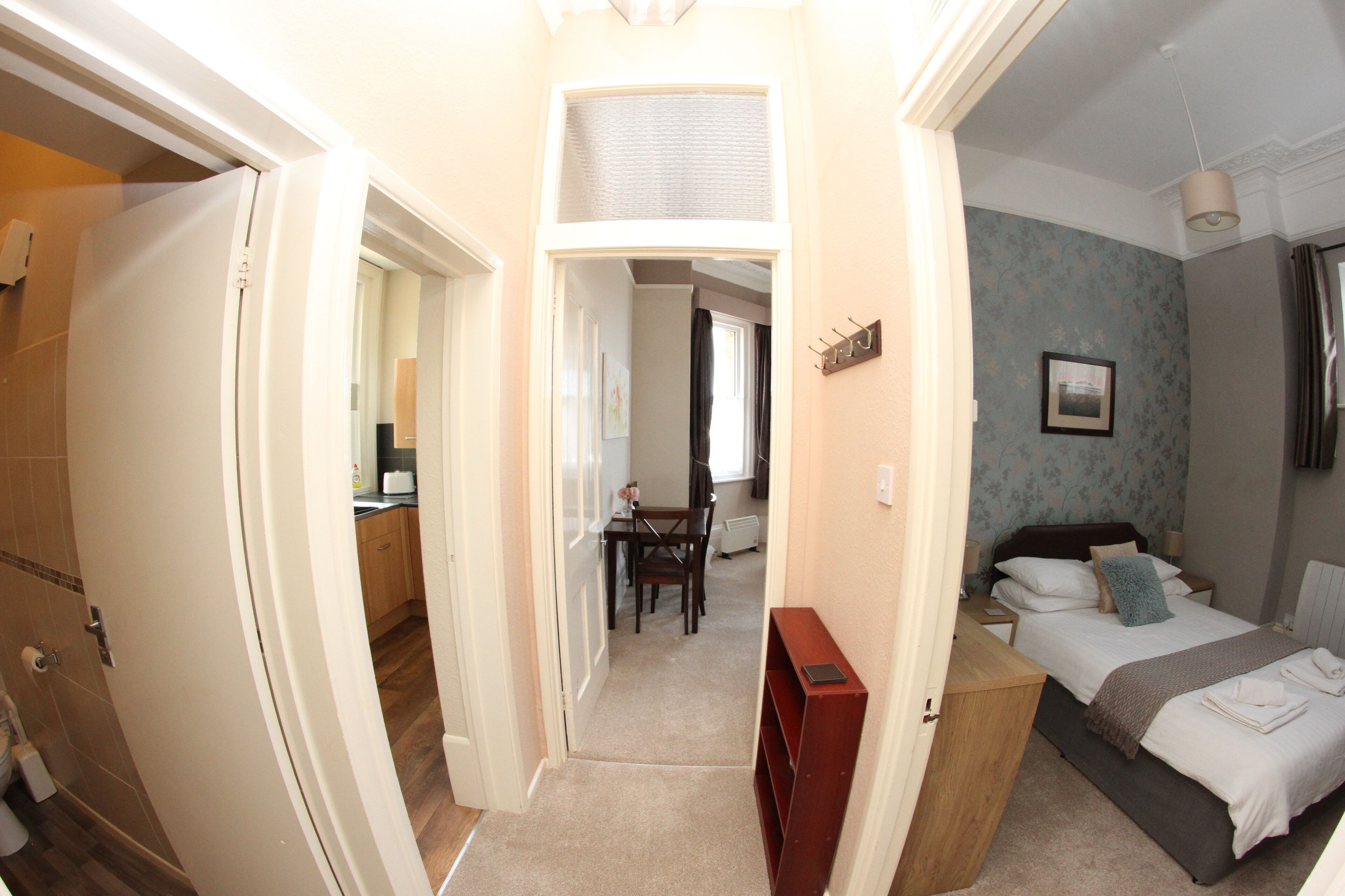 Une chambre à coucher comprenant un lit, une table de chevet et une commode. Un couloir mène à une salle de bain et à un coin repas.