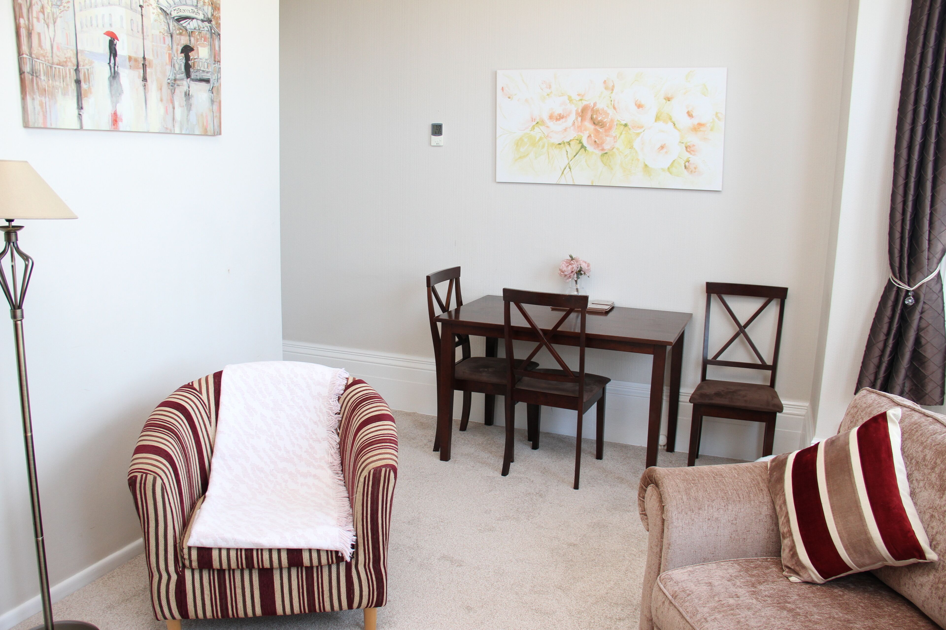 A living room with a striped sofa, a cushioned armchair, a dining table with chairs, and a painting on the wall.