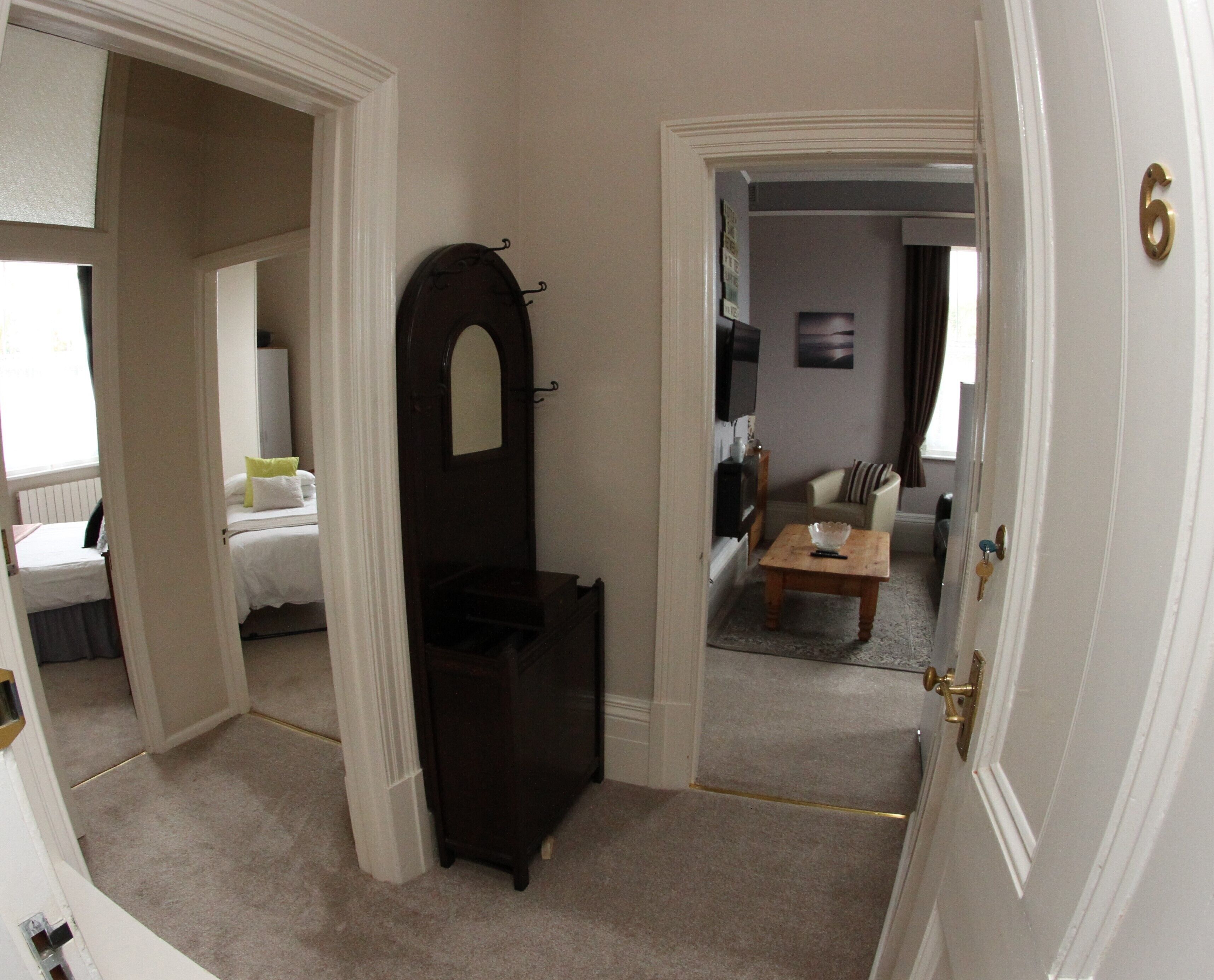A room with a bed, a dark wooden wardrobe, a small table, a sofa, and a television.